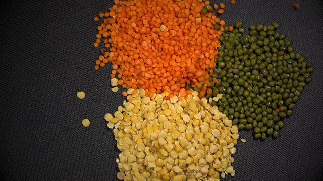 A rain from seeds drops on three bunches of lentils and mung in slow motion.
