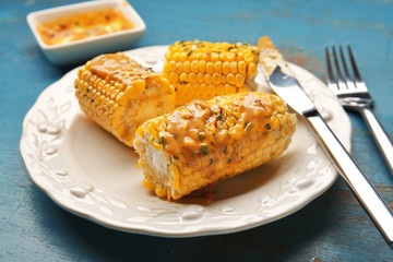 Plate with cut tasty grilled corncobs, sauce and herbs on wooden table, close up view
