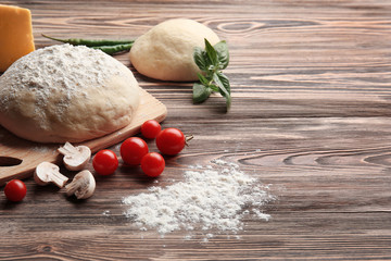 Raw pizza dough with ingredients on wooden table