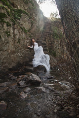 Young woman with blue eyes dressed bride sitting on a stone stairs in the countryside near a river just before marriage. 