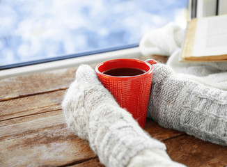 Human hands holding cup of coffee on windowsill