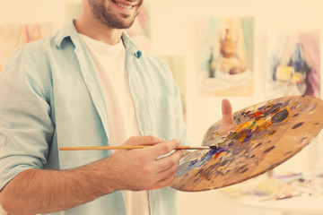 Young male artist with palette and brush in studio, close up