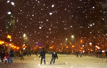 Winter night in Chicago. People enjoying ice skating at Millennium park ice rink during snowy night...