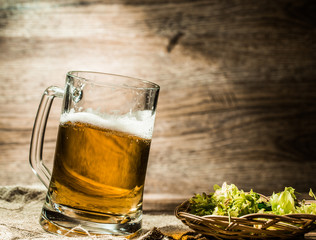Big mug of beer stands on linen cloth with hops
