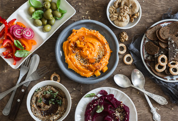 Vegetarian snack. Pumpkin, beets hummus, beans and mushroom pate, vegetables, nuts, bread on a wooden table, top view. Flat lay. Vegetarian, healthy food concept