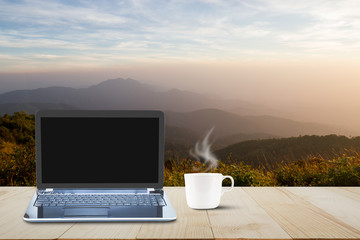 Hot coffee cup with steam on vintage wooden table top on blurred meadow and foggy mountain...