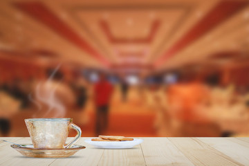 Hot coffee cup with steam on vintage wooden table top on hotel lobby background