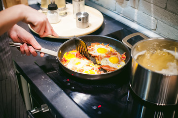 Woman puts homemade food. Female hands carefully applied to fried egg dish from  pan. breakfast for two persons, at home in kitchen at dining table