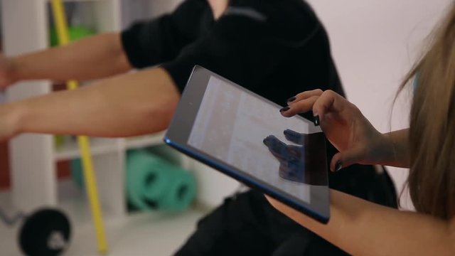 Athlete doing physical exercise, personal ems training in the gym with a trainer, which uses tablet