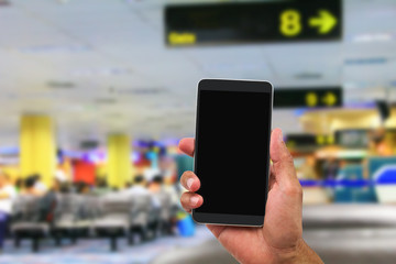 Man's hand holding mobile phone on blurred departure hall in airport