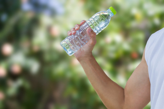 Man wearing white fitness sleeveless shirt holding plastic water bottle on blurred green bokeh background