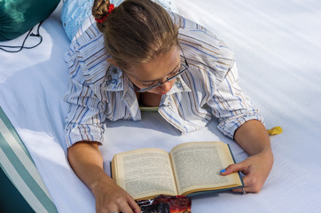 Fototapeta na wymiar Girl with glasses reading a book, lying on an air mattress