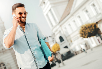 Handsome young man talking on the mobile phone and holding folde