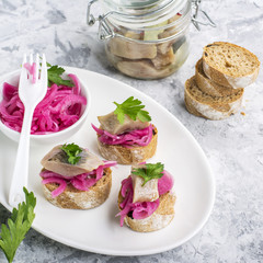 Finger snack. Mini open sandwiches with sweet pickled red onion, salt herring and greens on a light marble background. Top view.