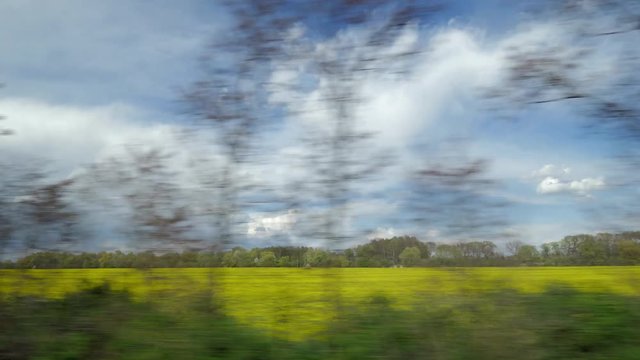 View from driving train window of countryside landscape, along yellow field against cloudy sky, Prague, Czech Republic