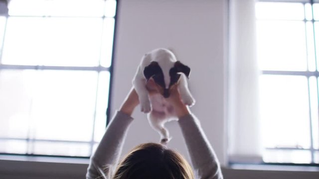 4K Young woman lifts her puppy and rests him on her chest as she strokes and plays with him, in slow motion