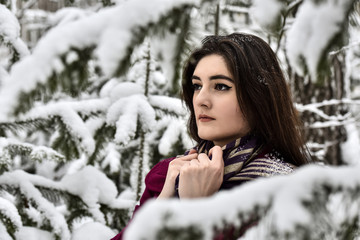 Girl in a red coat and headscarf on the background of snow-covered trees