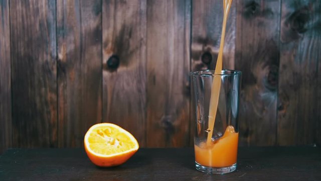 Orange Juice is Poured into a Glass on a Wooden Background. Slow Motion