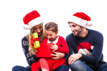 Young daughter open Christmas gift near mother and father on white background.