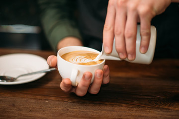 Closeup of male hands adding cream to coffee.
