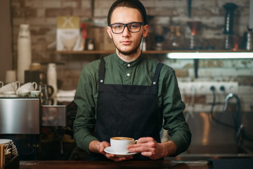 Waiter in black apron stretches a cup of coffee