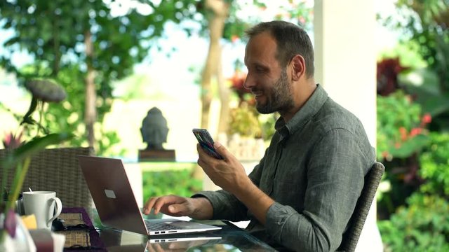 Happy, Young Man Working On Smartphone And Laptop In Garden 
