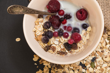 Bowl of muesli with frozen berries and plant milk, on black background.