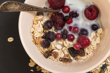 Bowl of muesli with frozen berries and plant milk, on black background.