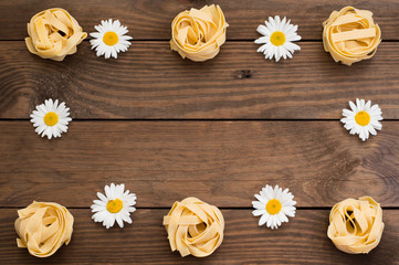 Raw fettuccine with flowers on wooden background. Italian Cuisine. Top view. Close-up