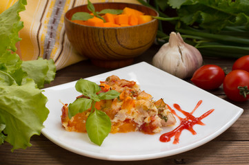 Casserole with chicken and pumpkin on a white square plate. Wooden rustic background. Close-up