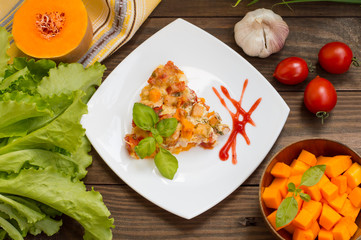 Casserole with chicken and pumpkin on a white square plate. Wooden rustic background. Top view. Close-up