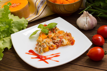 Casserole with chicken and pumpkin on a white square plate. Wooden rustic background. Close-up