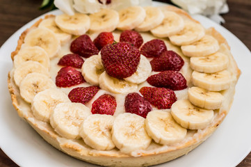 Tart with strawberries, bananas and whipped cream on a background of flowers. Top view. Close-up