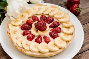 Tart with strawberries, bananas and whipped cream on a background of flowers. Top view. Close-up