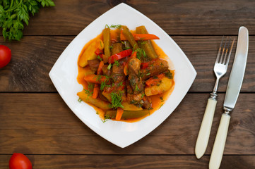 Stew with potatoes, carrots, pickles, tomatoes and hot peppers. Azu by Tartarian on a white square plate. Wooden rustic background. Top view. Close-up