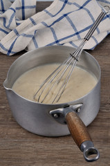 Casserole de sauce béchamel avec un fouet de cuisine et un torchon
