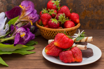 Strawberries with chocolate on a background of flowers. Wooden table. Close-up