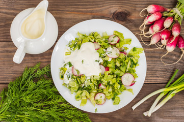 Salad with radishes, lettuce, spinach and sour cream on a wooden table. Close-up