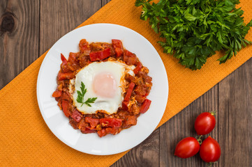 Shakshuka on a white plate. Traditional Jewish dish. Wooden table. Top view. Close-up