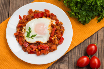 Shakshuka on a white plate. Traditional Jewish dish. Wooden table. Top view. Close-up