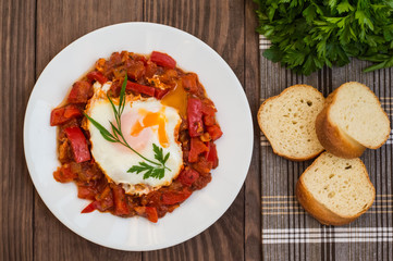 Shakshuka on a white plate. Traditional Jewish dish. Wooden table. Top view. Close-up