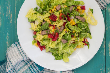 Salad from beef tongue, Chinese cabbage, peppers, corn, parsley and basil. Wooden background. Top view