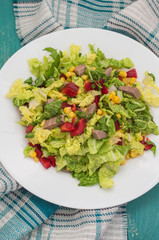 Salad from beef tongue, Chinese cabbage, peppers, corn, parsley and basil. Wooden background. Top view