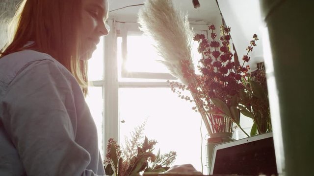 sunny view of florist arranging bunch of flowers near laptop