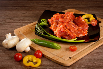 raw skewers of pork,lies on the black plate next to vegetables