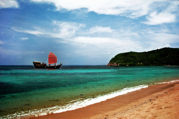 Sailboat with red sails in a tropical bay