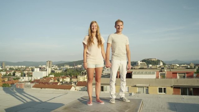 CLOSE UP: Happy young couple standing on the rooftop holding hands and smiling