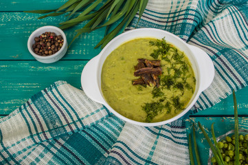 Puree soup with peas, melted cheese, roasted meat, croutons and herbs. Wooden background. Top view. Close-up