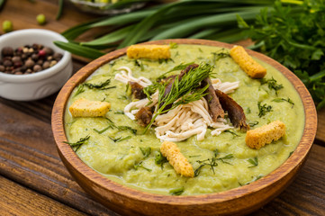Puree soup with peas, melted cheese, roasted meat, croutons and herbs. Wooden background. Top view. Close-up