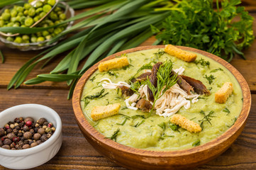 Puree soup with peas, melted cheese, roasted meat, croutons and herbs. Wooden background. Top view. Close-up